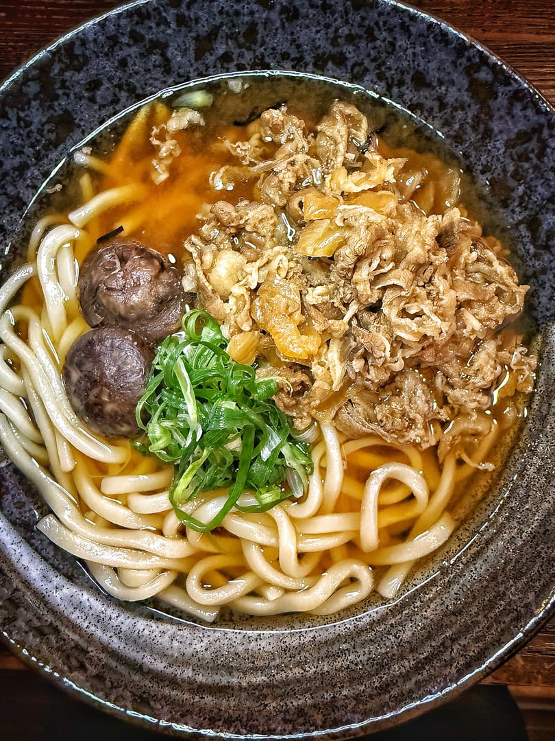 A bowl of udon noodles with beef, mushrooms, and green onions in a savory broth.